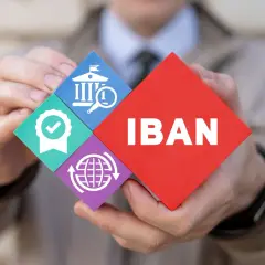 Ręce trzymają puzzle z napisem IBAN i ikonami: bank, certyfikat, globalna sieć.