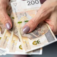 Dłonie trzymające stos banknotów 200 zł. Pieniądze mogą symbolizować oszczędności na przyszłość, np. na okresową emeryturę kapitałową.