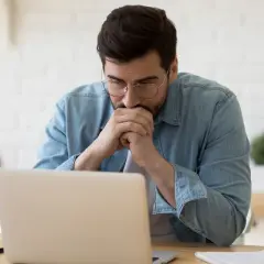 Zamyślony mężczyzna przy laptopie, analizuje składkę zdrowotną ryczałt 2024.