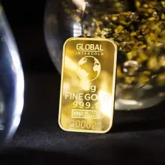 Sztabka 50g czystego złota 999.9, błyszcząca na tle szkła z płatkami złota.