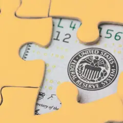 Żółte elementy układanki odsłaniają fragment banknotu stu dolarowego, symbolizując złożoność finansów i merkantylizm.