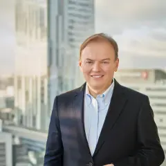 Uśmiechnięty mężczyzna w garniturze, cfo, stoi na tle nowoczesnych wieżowców.