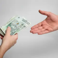 Dłoń podaje plik banknotów 100 zł. Zastanawiasz się, ile wynoszą odsetki od niezapłaconej faktury?