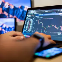 Osoba analizuje wykresy na laptopie, ucząc się, day trading co to jest. Obok leży smartfon.
