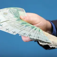 Dłoń trzyma plik banknotów 100 zł. Zastanawiasz się, co z pieniędzmi z OFE po przejściu na emeryturę?