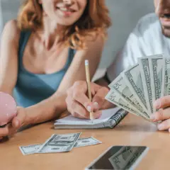 Para trzymająca skarbonkę i pieniądze, pisząca w notatniku.