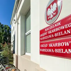 Tablice Urzędu Skarbowego Warszawa-Bielany. Obok stoją rowery, a w tle drzewa i błękitne niebo. sd-z2.
