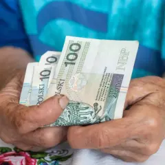 Dłonie starszej osoby trzymają banknoty 100 zł. Czy to wystarczy na najniższą emeryturę 2026?