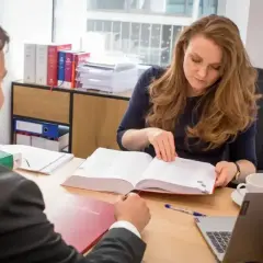 Kobieta z rudymi włosami, pełniąca rolę zarządcy sukcesyjnego, przegląda dokumenty z mężczyzną w garniturze.