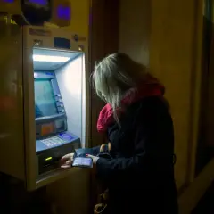 Kobieta przy bankomacie, wyciąga kartę. To symboliczny obraz mnożnika kreacji pieniądza w obiegu.
