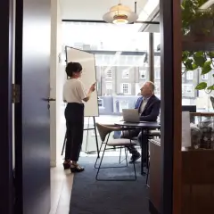 Kobieta przy tablicy omawia strategię sanacji z mężczyzną przy laptopie.