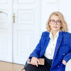 Kobieta w okularach i niebieskiej marynarce trzyma notatnik. Planujesz otwarcie firmy w 2025? Sprawdź dostępne dotacje!