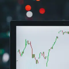 Wykres świecowy na ekranie laptopa pokazuje zmienny kurs USD JPY. W tle rozmyte światła miasta.