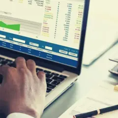 Ręce na klawiaturze laptopa, na ekranie wykresy i tabele z danymi finansowymi, widoczne są też przyciski "SUBMIT" i "CLEAR", sugerujące pracę nad transakcjami, być może w kontekście giełdowym lub analizy danych, np. w eps.