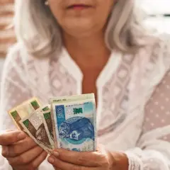 Kobieta z siwymi włosami trzyma polskie banknoty. To symbol oszczędności na emeryturę kapitałową dla kobiet.