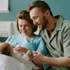 Szczęśliwi rodzice patrzą na noworodka. To dla niego czeka becikowe, symbol miłości i wsparcia.