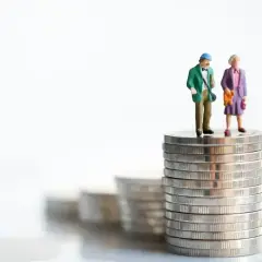 Figurki starszej pary stoją na stosie monet, symbolizując pytanie: ile wynosi renta rodzinna?