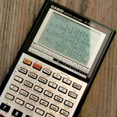 Kalkulator naukowy Casio fx-7000G na drewnianym blacie, wyświetla wyniki obliczeń.