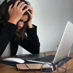 Kobieta z rękami na głowie przy laptopie, wyrażająca frustrację. To może być moment przed podjęciem decyzji o porzuceniu pracy.
