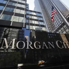 Błyszczący napis JP Morgan Chase & Co na tle drapaczy chmur i amerykańskiej flagi.