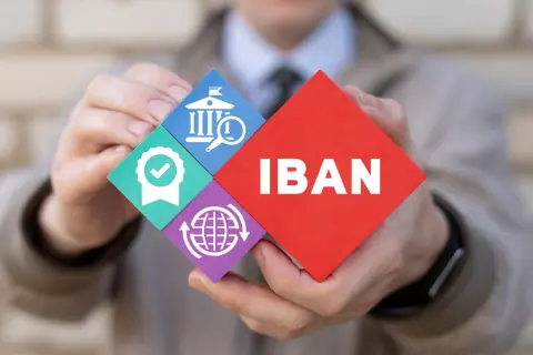 Ręce trzymają puzzle z napisem IBAN i ikonami: bank, certyfikat, globalna sieć.