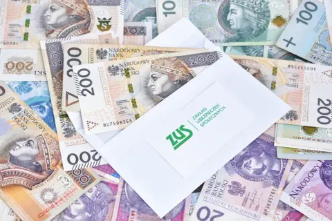 Zasiłki przedemerytalne po nowemu: koperta ZUS na stosie polskich banknotów 200 zł.