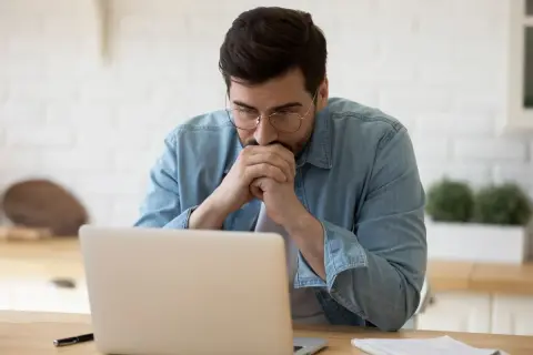 Zamyślony mężczyzna przy laptopie, analizuje składkę zdrowotną ryczałt 2024.