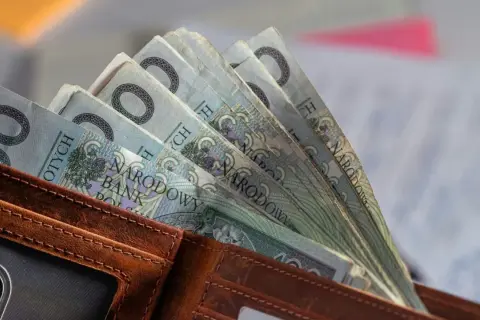 Portfel z polskimi banknotami 100 zł. W tle dokumenty, być może związane ze świadczeniem pielęgnacyjnym 2026.