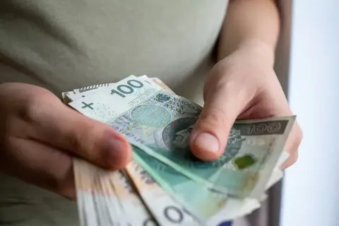 Dłonie trzymające stos banknotów 100 zł. Może to być pomoc de minimis dla przedsiębiorcy.