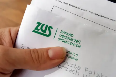 Dłoń trzyma dokument z zielonym logo ZUS. To pismo z Zakładu Ubezpieczeń Społecznych, które może dotyczyć spraw związanych z ubezpieczeniem.