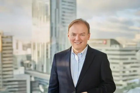 Uśmiechnięty mężczyzna w garniturze, cfo, stoi na tle nowoczesnych wieżowców.