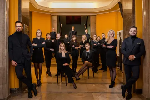 Grupa profesjonalistów w eleganckich czarnych strojach pozuje w holu.