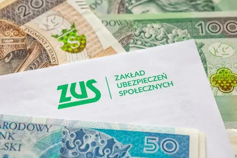 Kiedy ZUS wypłaca L4, pieniądze wreszcie się pojawiają. Koperta z logo ZUS na tle polskich banknotów.