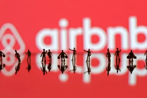 Małe figurki ludzi na tle logo Airbnb. Zastanawiasz się, airbnb co to? To platforma do rezerwacji noclegów i doświadczeń.