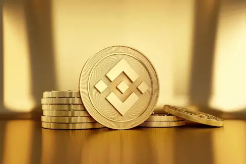 Złote monety z symbolem BNB, ułożone w stosy na błyszczącym, złotym tle.