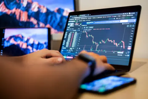 Osoba analizuje wykresy na laptopie, ucząc się, day trading co to jest. Obok leży smartfon.