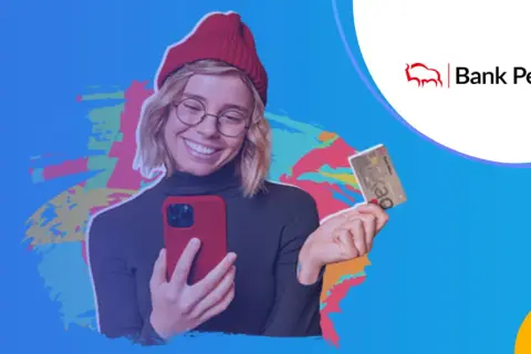 Uśmiechnięta młoda kobieta w czerwonej czapce trzyma telefon i kartę bankową Pekao.