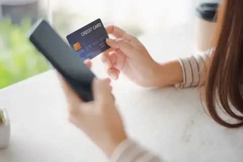 Kobieta trzyma kartę kredytową i telefon, przygotowując się do płatności online. W razie problemów z transakcją, może skorzystać z procedury chargeback.