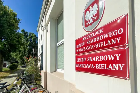 Tablice Urzędu Skarbowego Warszawa-Bielany. Obok stoją rowery, a w tle drzewa i błękitne niebo. sd-z2.