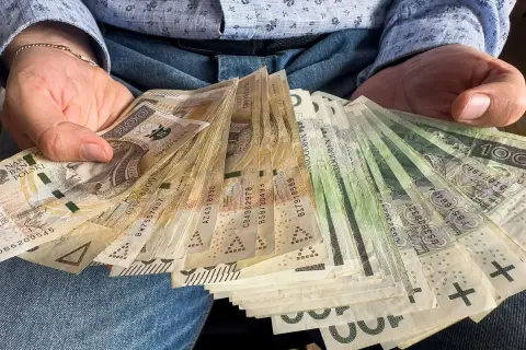 Ręce trzymające plik banknotów 1000 plus. Widać polskie złote, w tym nominały 100 i 200 zł.