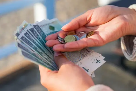 Dłonie liczą banknoty i monety. To może być świadczenie uzupełniające, które pomaga w codziennych wydatkach.