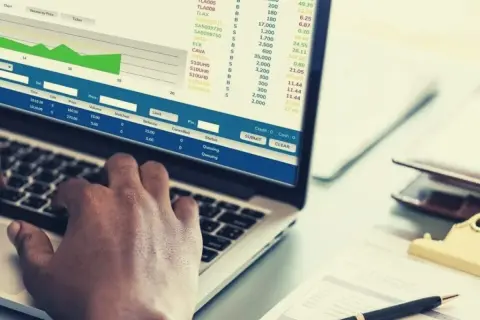 Ręce na klawiaturze laptopa, na ekranie wykresy i tabele z danymi finansowymi, widoczne są też przyciski "SUBMIT" i "CLEAR", sugerujące pracę nad transakcjami, być może w kontekście giełdowym lub analizy danych, np. w eps.