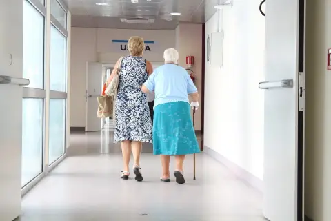 Dwie kobiety idą korytarzem szpitalnym. Jedna wspiera się laską. Być może zmierzają po świadczenia 500 plus dla chorych na raka ZUS.