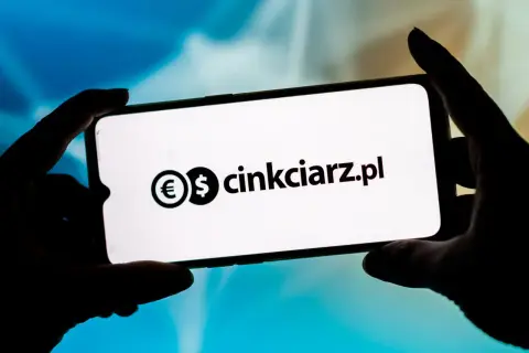Dłonie trzymają smartfon z widocznym logo i nazwą "cinkciarz.pl". To portal, który ułatwia wymianę walut, jak Conotoxia.