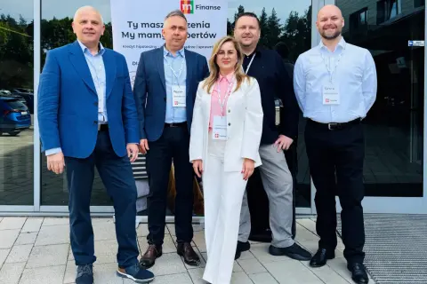 Pięć osób w eleganckich strojach stoi przed budynkiem, za nimi baner z logo "m Finanse".