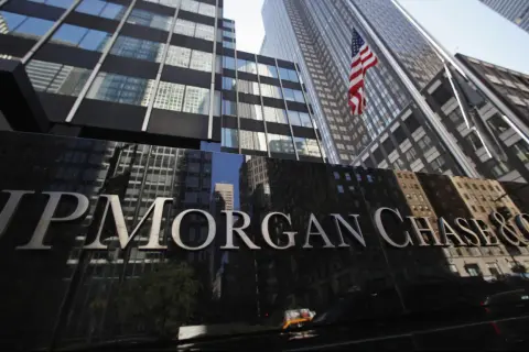 Błyszczący napis JP Morgan Chase & Co na tle drapaczy chmur i amerykańskiej flagi.