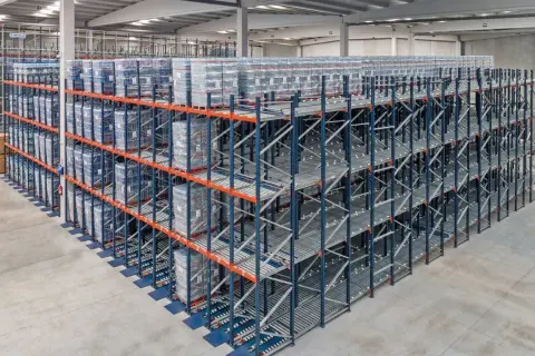 Duże regały magazynowe z towarami ułożonymi zgodnie z zasadą fifo. Towary na rolkach, gotowe do wysyłki.