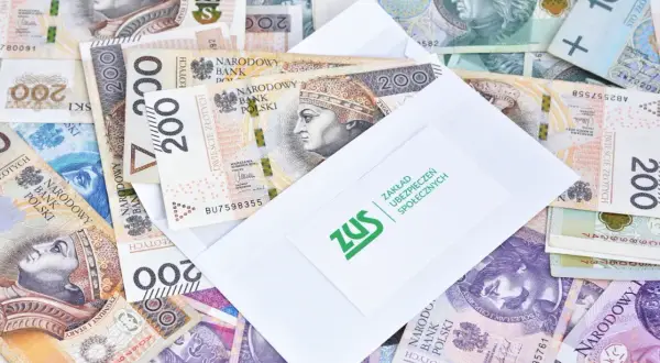 Zasiłki przedemerytalne po nowemu: koperta ZUS na stosie polskich banknotów 200 zł.