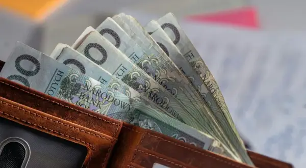 Portfel z polskimi banknotami 100 zł. W tle dokumenty, być może związane ze świadczeniem pielęgnacyjnym 2026.