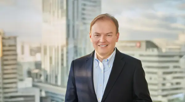 Uśmiechnięty mężczyzna w garniturze, cfo, stoi na tle nowoczesnych wieżowców.